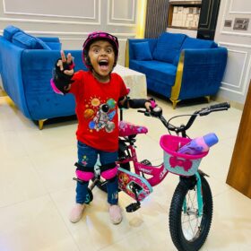 A happy child wearing a premium red kids’ t-shirt with a colorful space astronaut design, posing with a bicycle indoors.